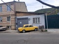 Old Yellow Zhiguli Lada Car in the Town of Gori, Georgia, on a Cloudy Day, with a Brick House and Mountains Royalty Free Stock Photo