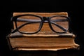 Old yellowed book and black glasses. Forgotten publications on the dark table Royalty Free Stock Photo