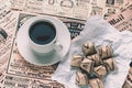 old yellowed newspapers with news and announcements are laid out on the table. Cup of coffee and waffle cookies wrapped in white