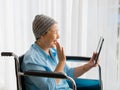 Older Asian woman patient covered the head with clothes effect from chemo treatment in cancer cure process waving hand to greeting