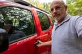 An older bald Caucasian male with his hand on the handle of a red sport utility vehicle