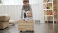 Older boy riding his baby brother in wooden toy cart in living room. Royalty Free Stock Photo