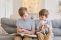 An older brother is reading book to his younger brother sitting on couch. Royalty Free Stock Photo