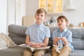 An older brother is reading book to his younger brother sitting on couch. Royalty Free Stock Photo