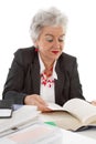 Older business woman sitting at desk reading in a book. Concept