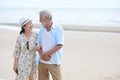Older couple caucasian husband and asian wife holding hand and resting and standing on sandy beach after retirement in resort