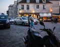 Older couple strolls across Montmartre square between motorcycles and taxis in evening
