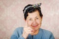 Older cute hispanic woman wearing blue sweater and flower pattern bow on head holding up one finger for the camera in