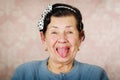 Older cute hispanic woman wearing blue sweater and polka dot bowtie on head showing her tongue to the camera in front of