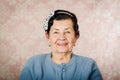 Older cute hispanic woman wearing blue sweater and polka dot bowtie on head smiling happily in front of pink wallpaper