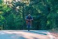 Older cyclist in his mid-40s riding a bike on a road through the woods and looking extremely tired