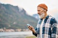 Older elder hipster man standing in nature park wearing earbud using phone.