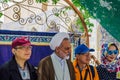 An older Iranian Mullah wearing a keffiyeh poses with tourists in the courtyard of the Jame Mosque