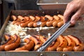 Hot dog sausages and onions grilling with hand turning Royalty Free Stock Photo