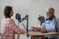 older man and female presenter in a recording studio create a podcast. senior, woman radio presenter or interviewer Royalty Free Stock Photo