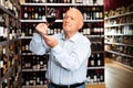 Older man inspecting quality of red wine in wine store in search of perfect wine for solemn occasion