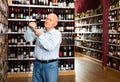 Older man inspecting quality of red wine in wine store in search of perfect wine for solemn occasion