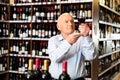 Older man inspecting quality of red wine in wine store in search of perfect wine for solemn occasion Royalty Free Stock Photo