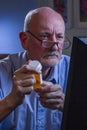 Older man looks concerned while refilling prescription online, vertical