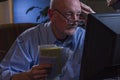Older man looks worried as he pays bills online, horizontal