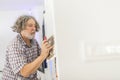 Older man plastering a wall as he fixates an orange corrugated p