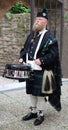 Older man, Scottish, with long beard and kilt, plays on a drum, and drumsticks, he has fu