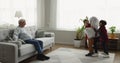 Older man sits on sofa, looks how his great-grandsons playing