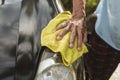 An older man uses a yellow washcloth to clean the hood of his black hatchback. A car owner washing his automobile outside first