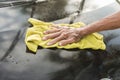 An older man uses a yellow washcloth to clean the hood of his black hatchback. A car owner washing his automobile outside first