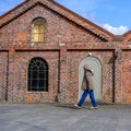 Older Man Walking Past A Traditional Brick Building Under A Blue Sky