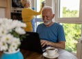 Older man working on laptop at homeand woman wiping windows Royalty Free Stock Photo