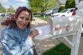 Older senior citizen woman smiles as she removes a blank white envelope from a white mailbox Royalty Free Stock Photo