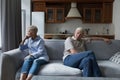 Older silent couple after quarrel sit on sofa apart