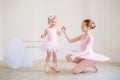 The older sister, a ballerina in a pink tutu and pointe shoes, shows the baby how to practice at the barre