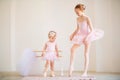 The older sister, a ballerina in a pink tutu and pointe shoes, shows the baby how to practice at the barre