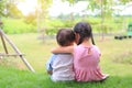 Older sister hugs little brother by the neck, shoulders sitting on green grass field. Two adorable Asian children sitting and