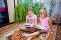 The older sister is reading a big book with fairy tales to her younger sister. Children play together at home Royalty Free Stock Photo