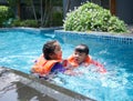 The older sister teach her younger brother how to swim with life jacket. Asian child playing in the swimming pool Royalty Free Stock Photo