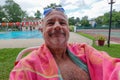 Older smiling caucasian man wearing a towel sitting by a pool with goggles and water droplets on his bald head Royalty Free Stock Photo