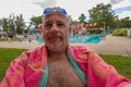 Older smiling caucasian man wearing a towel sitting by a pool with goggles and water droplets on his bald head Royalty Free Stock Photo