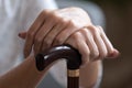 Older woman holding hands on wooden walking stick close up