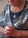 Older woman praying with linked hands and a gold medallion with the Virgin