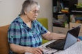 An older woman sits at a laptop. Mastering the older generation of technology by people. Internet communication from home, the