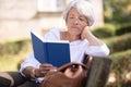 older woman sitting in park on bench reading book Royalty Free Stock Photo