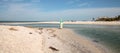 Older woman stands on the white sand beach in front of aqua blue