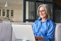 Older 60 woman using computer technologies at home sitting on sofa. Royalty Free Stock Photo