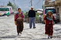 Older women in national clothes carry baskets along the street, behind them is a middle-aged man
