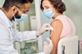 Older senior woman wearing face mask getting vaccination injection.