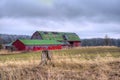 Red and green barn in the farm field under a cloudy sky.