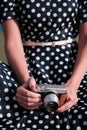 Oldschool mirrorless camera in the hands of a girl in a white and black dot dress